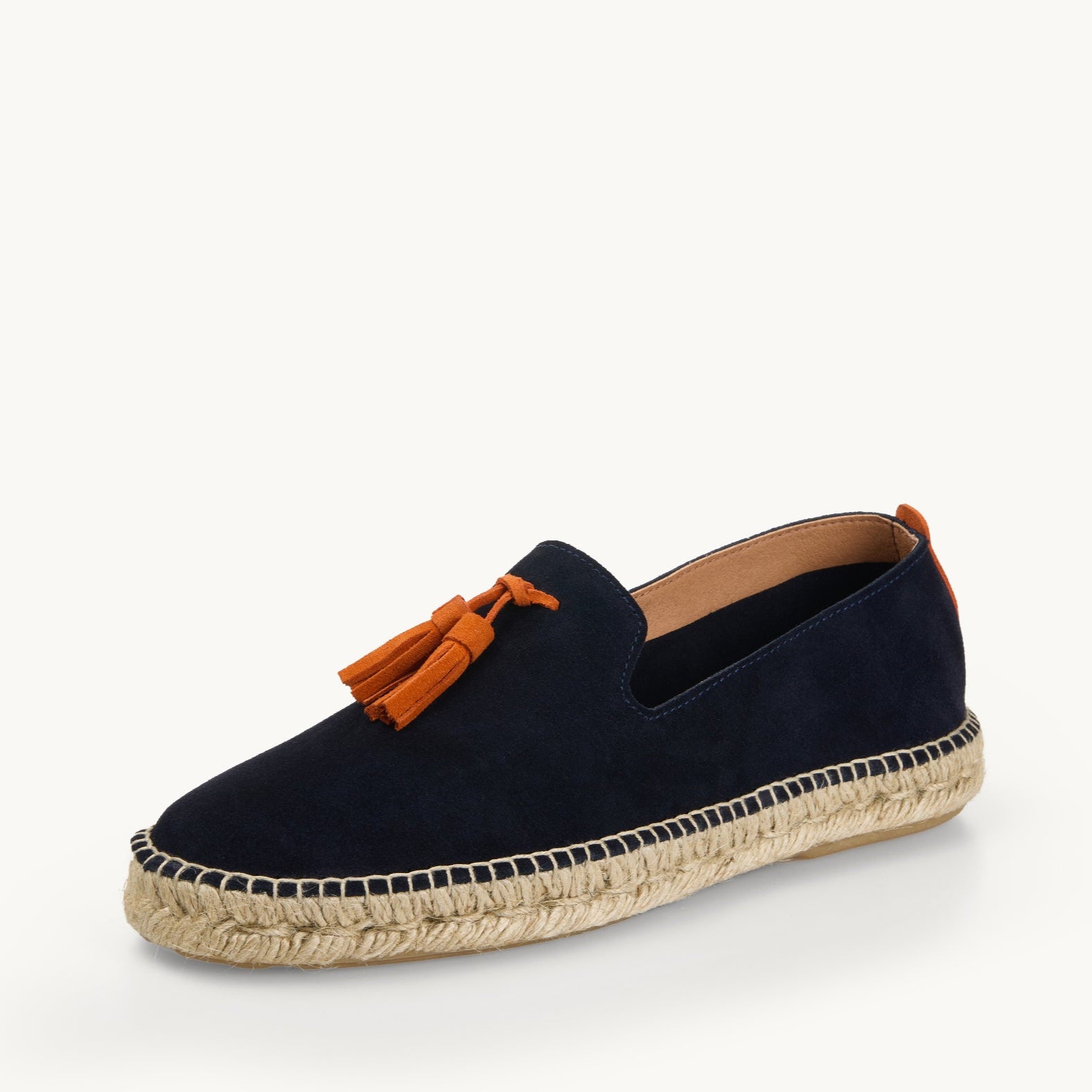One men's navy blue suede loafer. Jute sole. Neck opening of the espadrille has a narrow tan edged inside the shoe. Two orange suede tassel on the front.