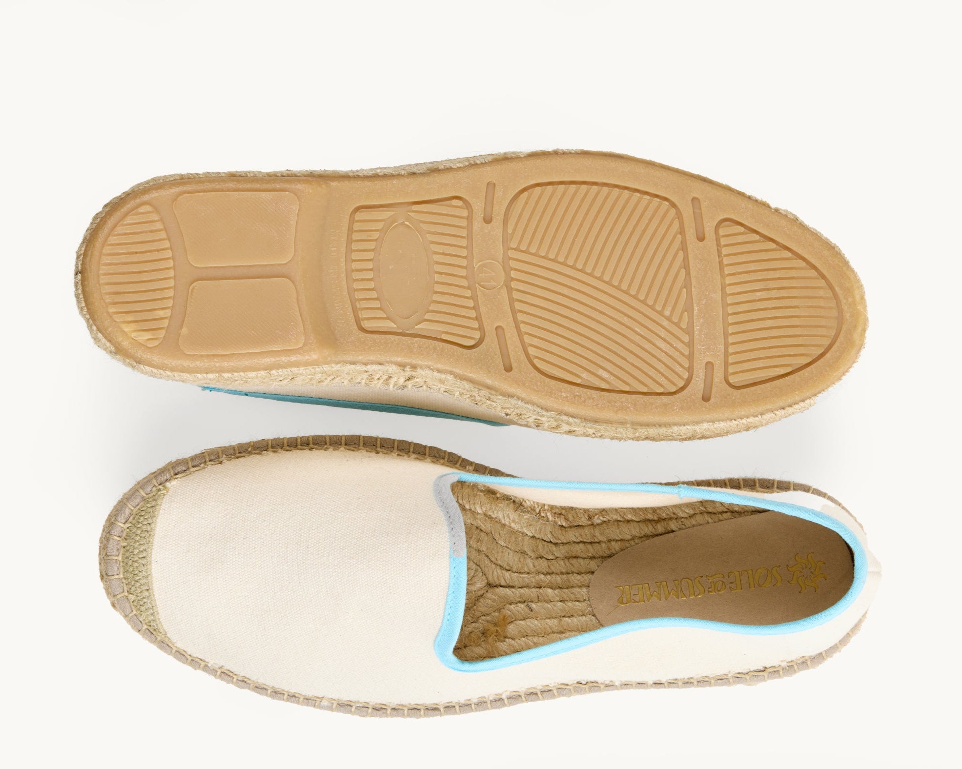 A pair of men's white cotton loafer espadrilles, the opening of the shoe is edged in a narrow light blue. One of the footwear is turned over to show the underneath. It has a full rubber covering and the other shoe shows the inner, unlined jute insole and the Sole of Summer logo printed on a small piece of cream suede.
