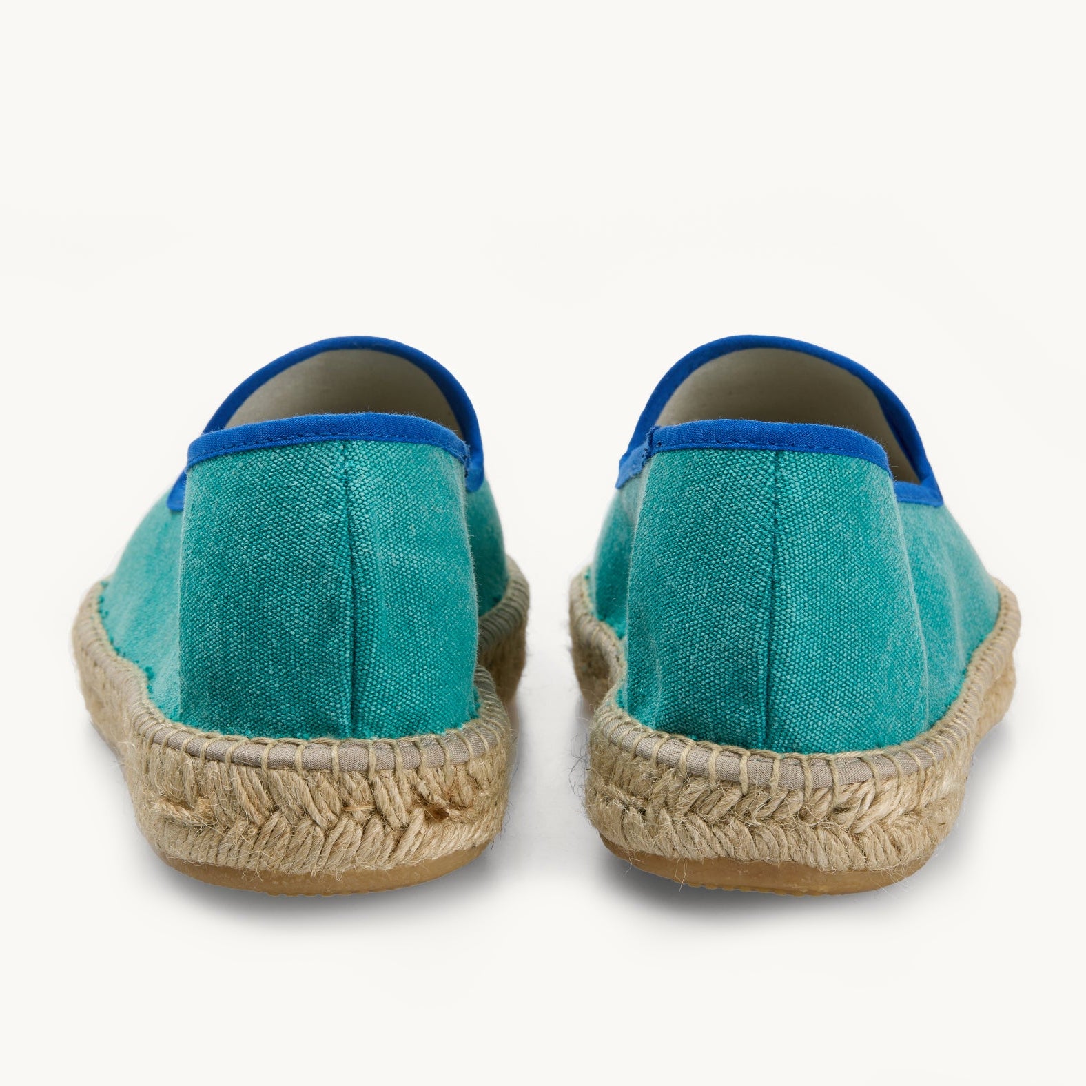 Pair of men's green cotton canvas loafers. View only of the heels. Jute sole. The neck opening of the espadrille has a narrow ribbon edged in royal blue. Inside of the footwear is white.