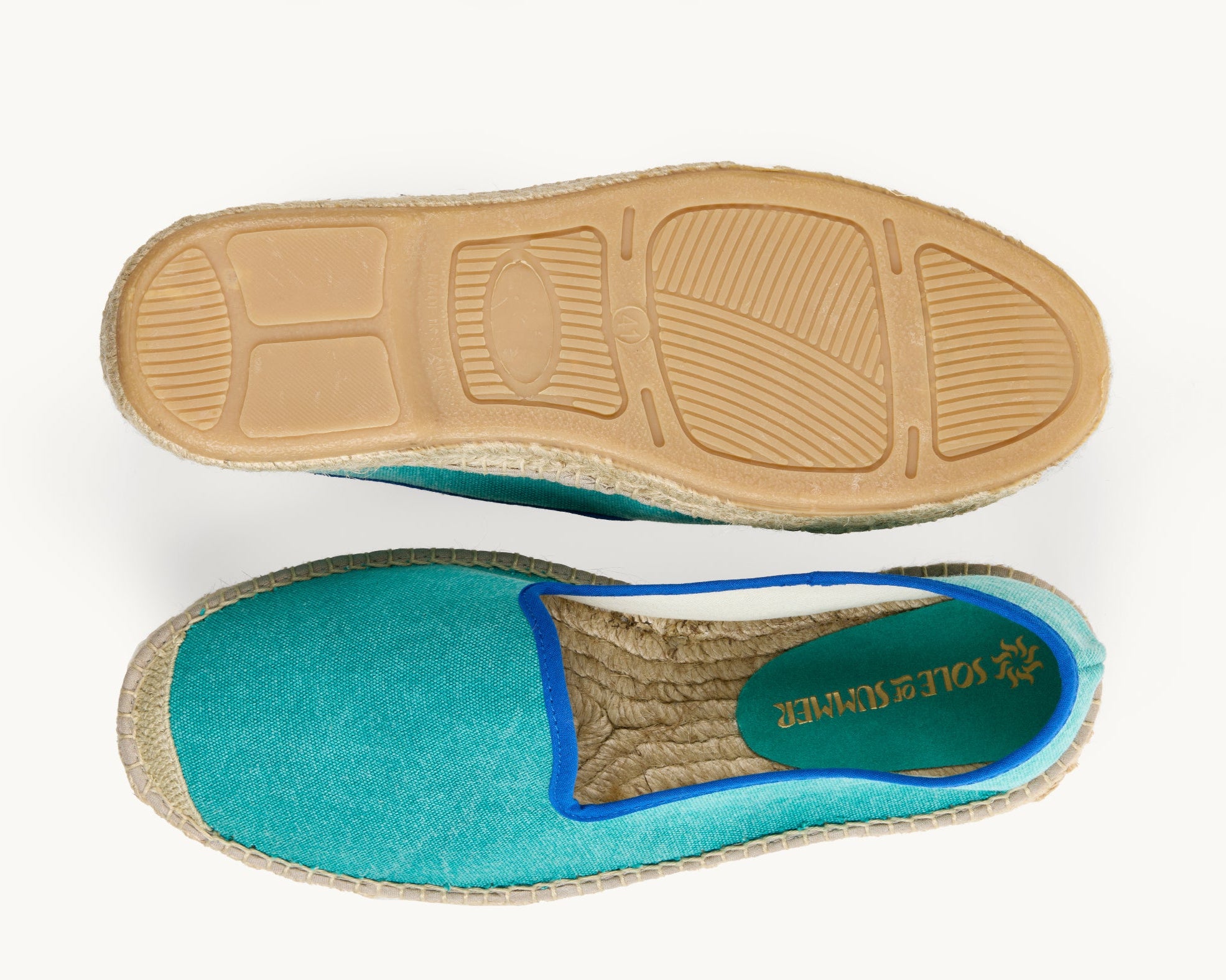 A pair of men's green cotton loafer espadrilles, the opening of the shoe is edged in a narrow royal blue ribbon. One of the footwear is turned over to show the underneath. It has a full rubber covering and the other shoe shows the inner, unlined jute insole and the Sole of Summer logo printed on a small piece of green suede.