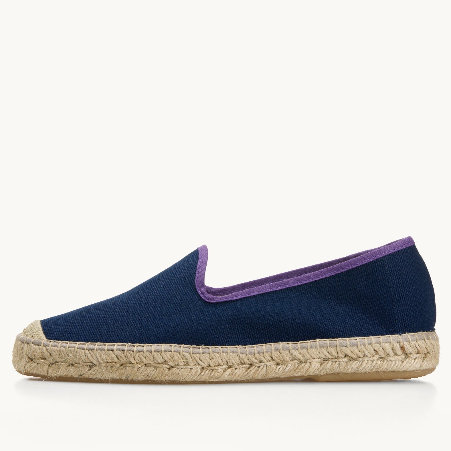 One men's navy blue cotton canvas loafer, side view. Jute sole and detail on the toe. Neck opening of the espadrille has a narrow ribbon edged in dark purple.