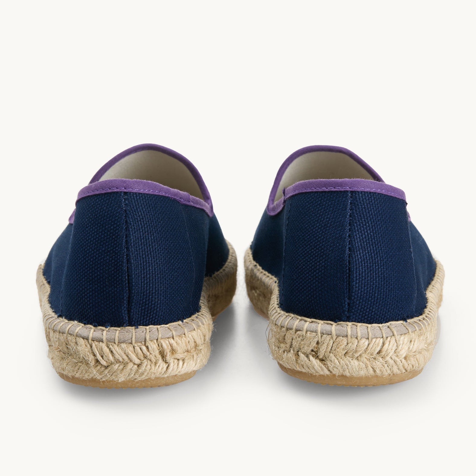 Pair of men's navy blue cotton canvas loafers. View only of the heels. Jute sole. The neck opening of the espadrille has a narrow ribbon edged in dark purple. Inside of the footwear is white.