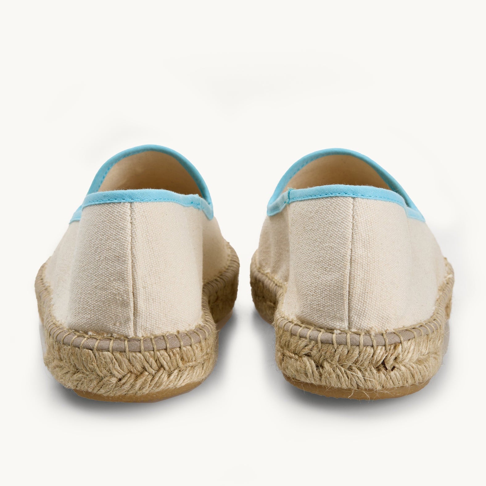 Pair of men's white cotton canvas loafers. View only of the heels. Jute sole. The neck opening of the espadrille has a narrow ribbon edged in light blue. Inside of the footwear is white.