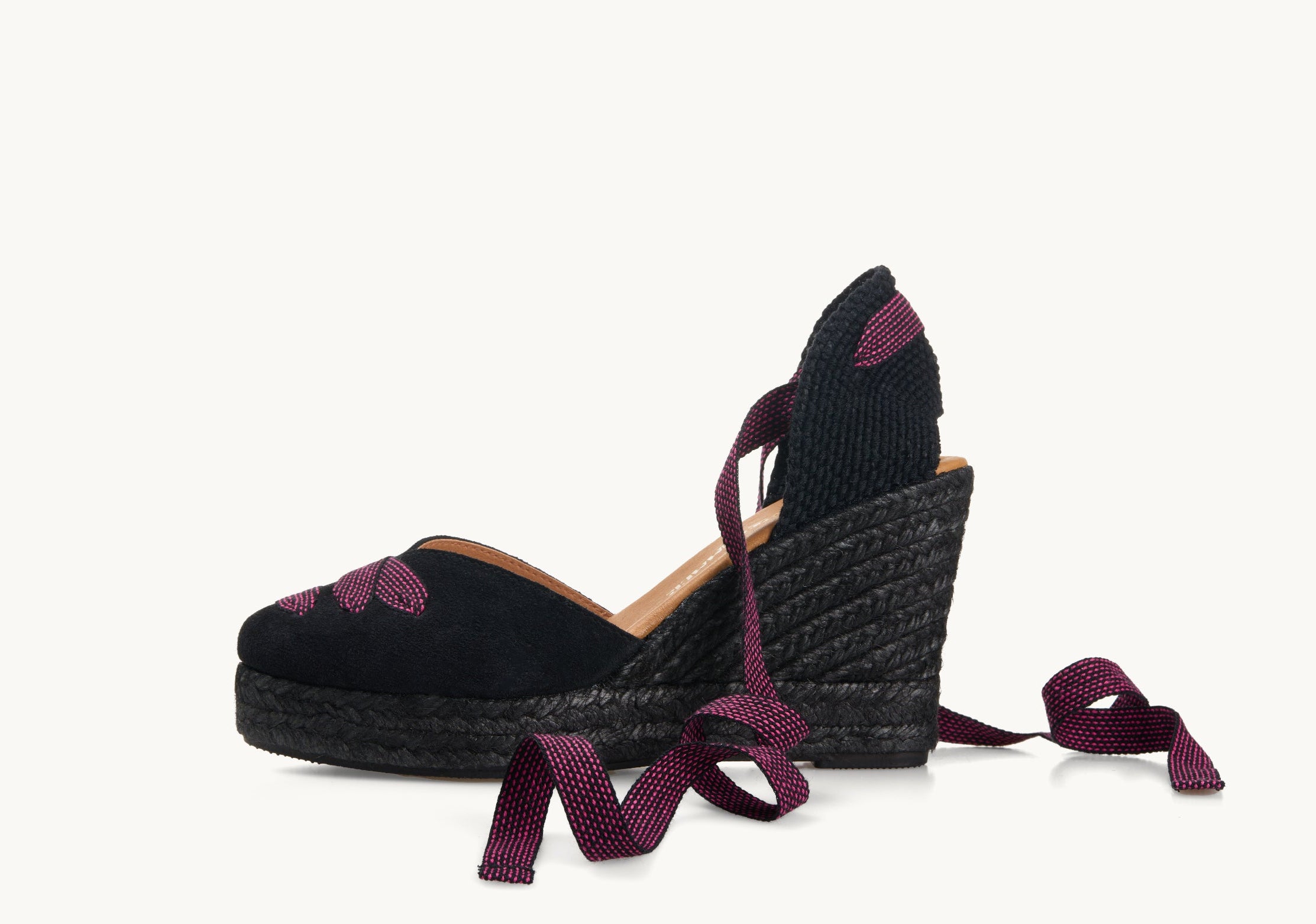 One black suede wedge espadrille shoe, side view. It has a black jute sole. Across the almond shaped toe is a criss-cross of black ribbon with pink dot pattern. The ankle ties are in the same ribbon material and are untied and loose to the side.