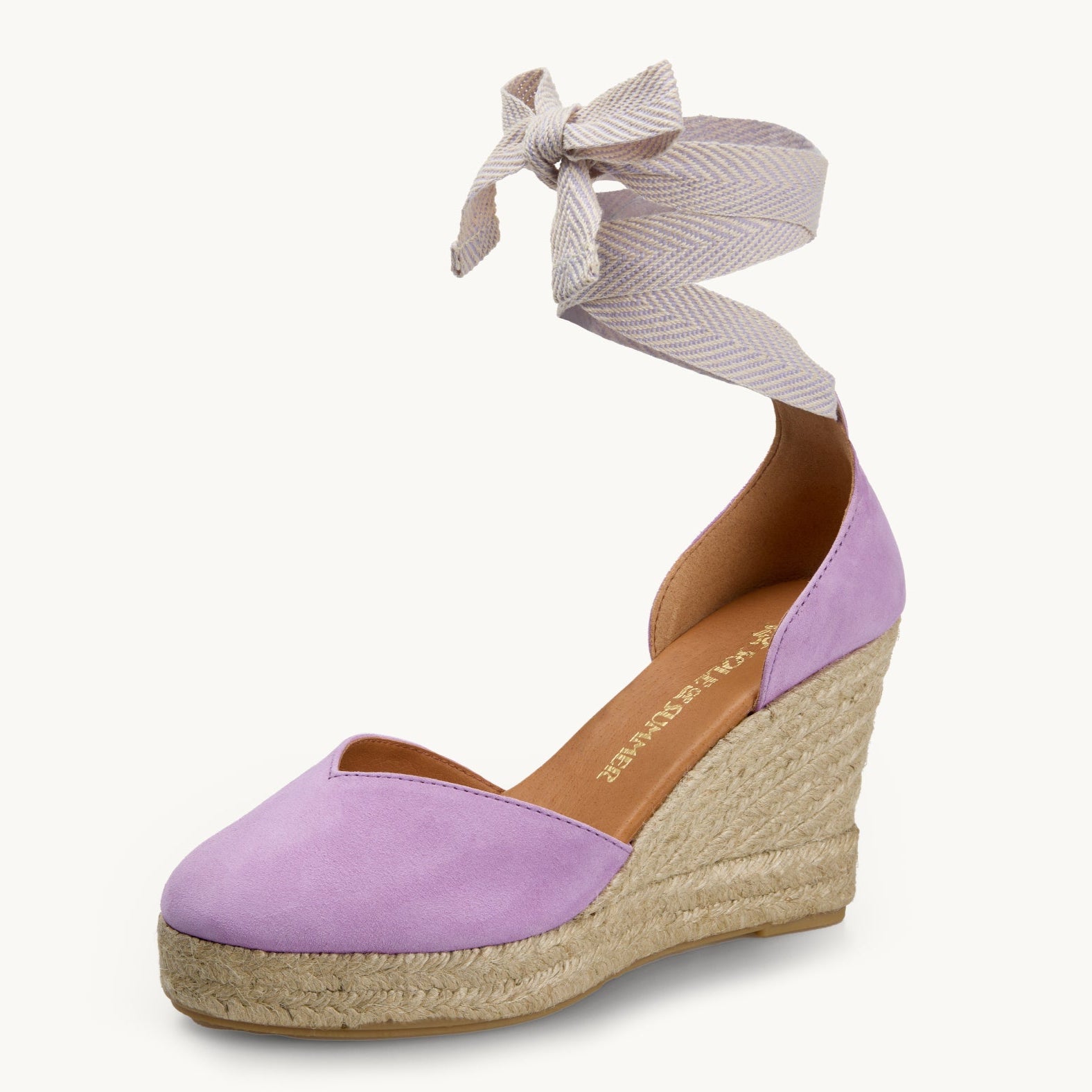 One lilac suede wedge espadrille displayed with white and lilac herringbone pattern ribbons tied in a bow as if around an ankle.  The sole is made of Jute. It has an almond shaped toe. The insole is lined in the tan leather and has a gold Sole of Summer logo printed on it.