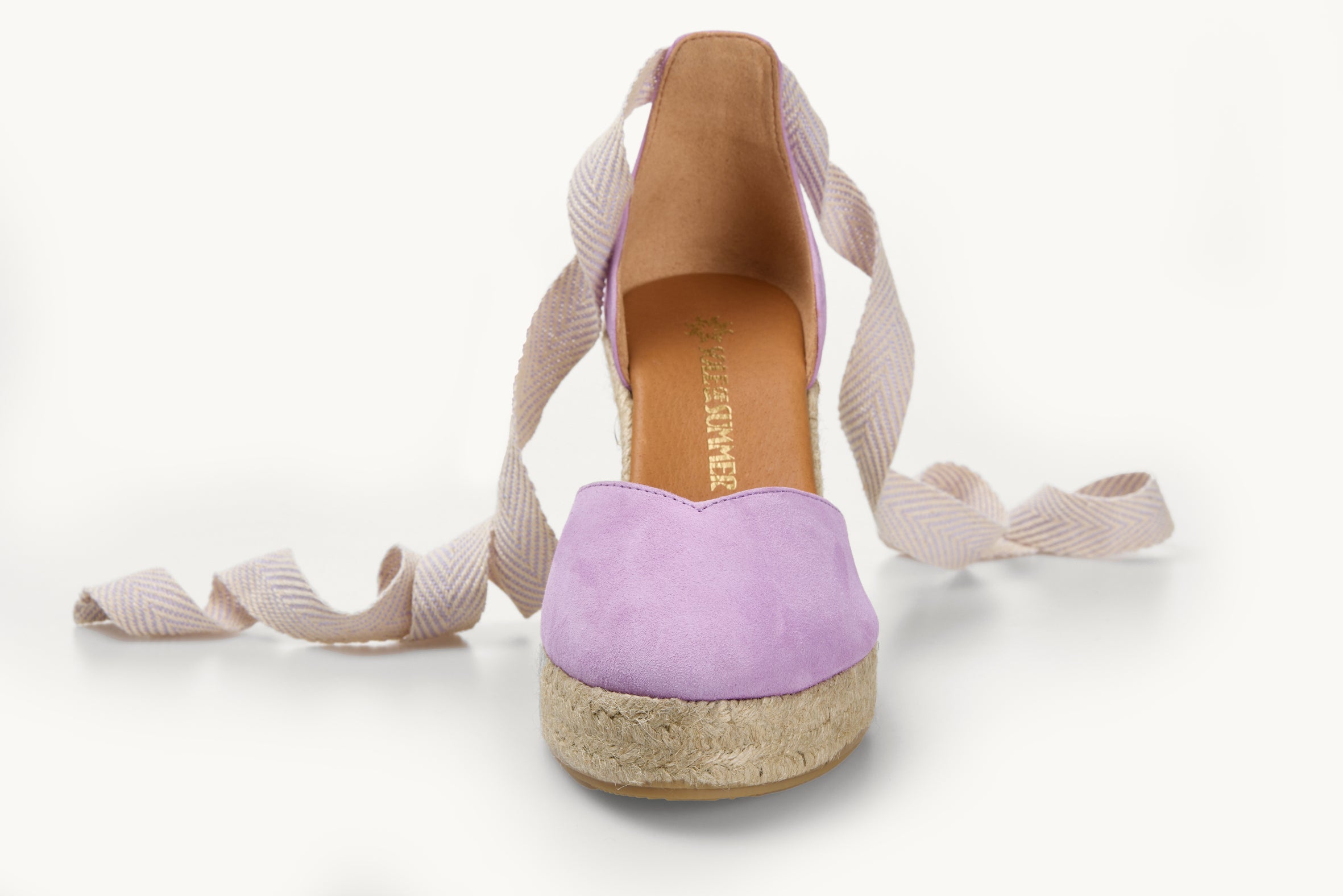One lilac suede wedge espadrille displayed with white and lilac herringbone pattern ribbons at the heel, left loose and untied on either side. The base is made of Jute. The toe is almond shaped.