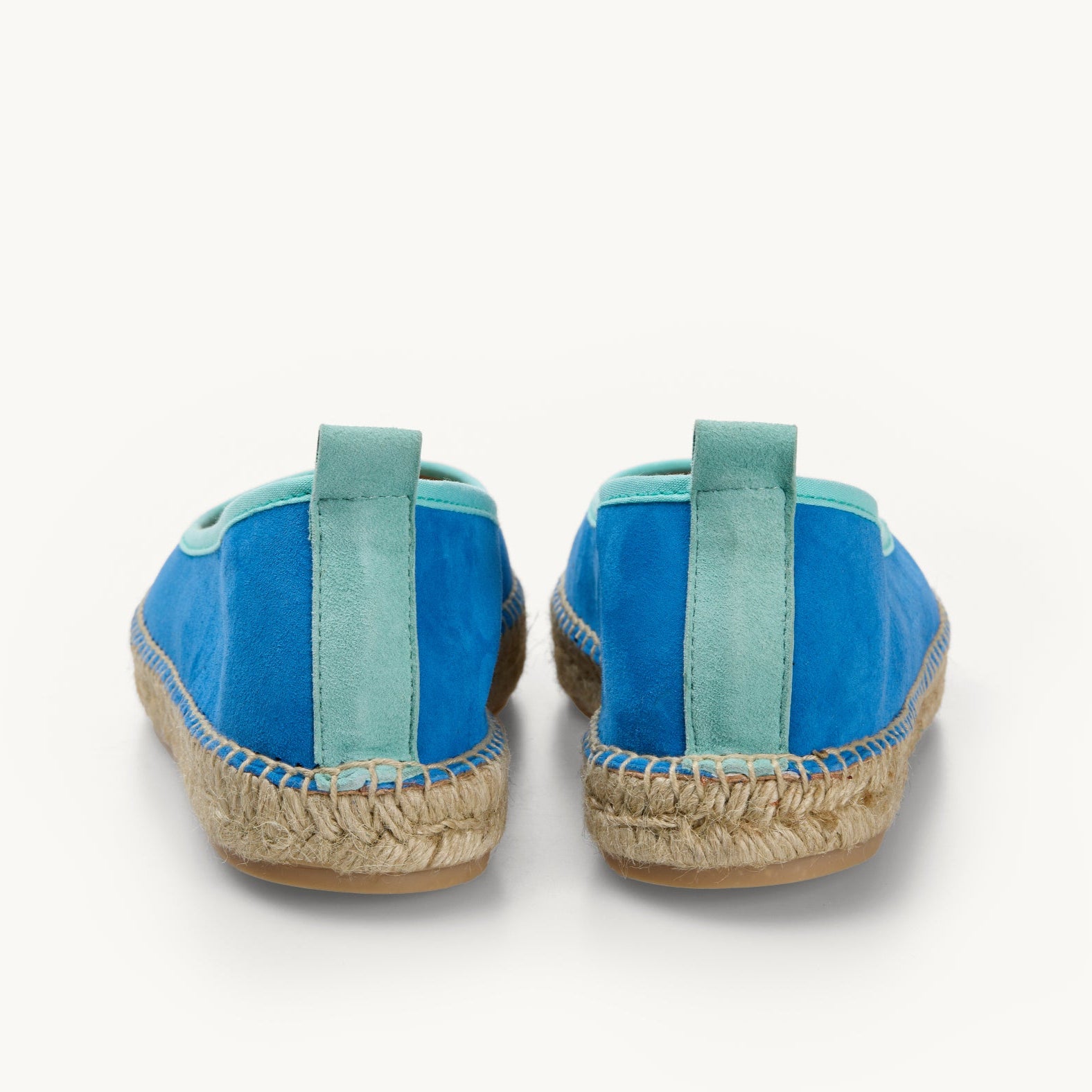 A pair of women's ballet flat espadrilles, only the heels are shown to highlight the detailing on the back. A duck egg turquoise suede stripe, approximately 1 centimetre wide, up the back of the azure blue shoes with stitched edge joining the upper to the a traditional jute sole.