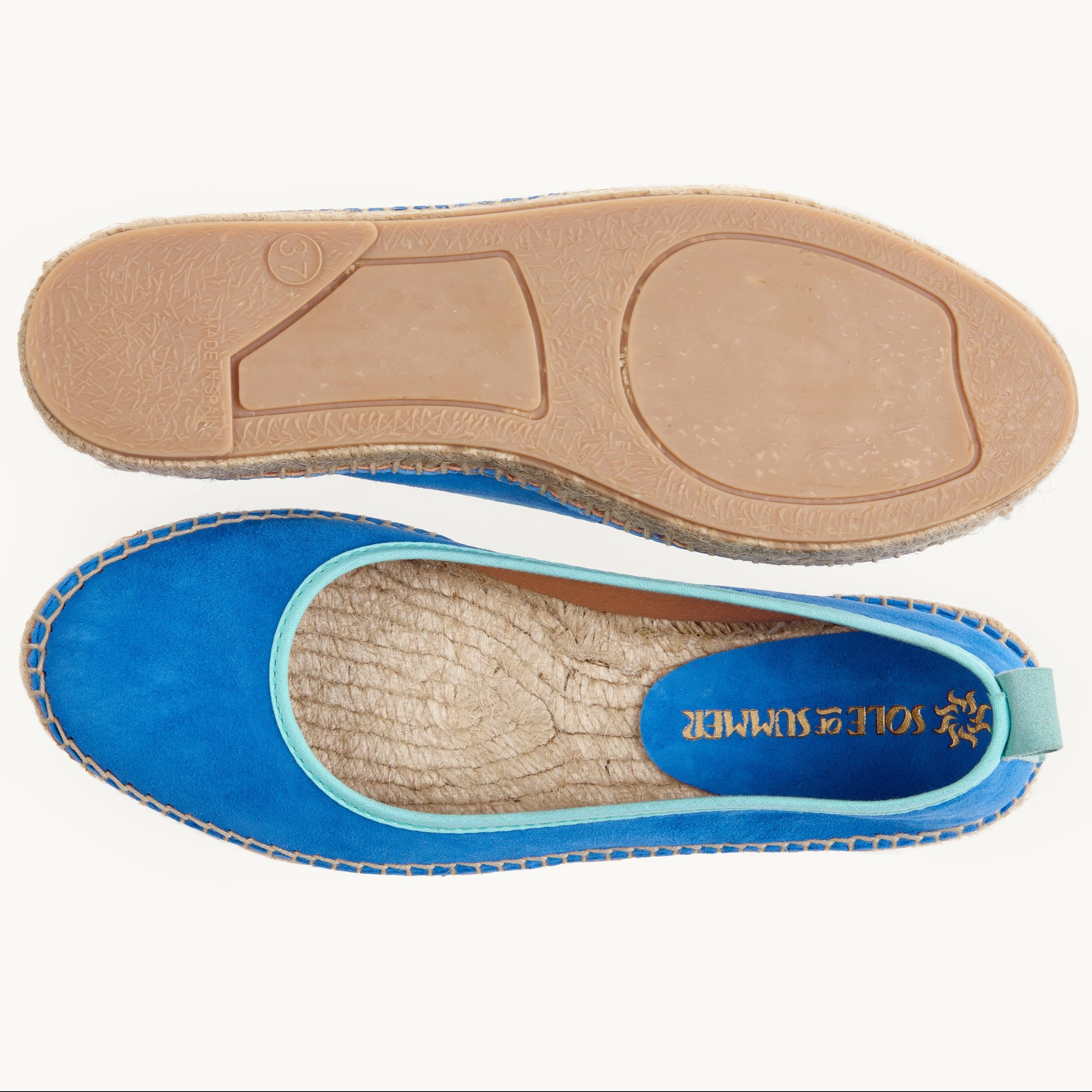 A pair of women's Azure blue suede flat ballet espadrilles. One of the shoes is turned over to show the underneath. It has a full rubber covering and the other shoe shows the inner of the footwear, unlined jute insole and the Sole of Summer logo printed inside.