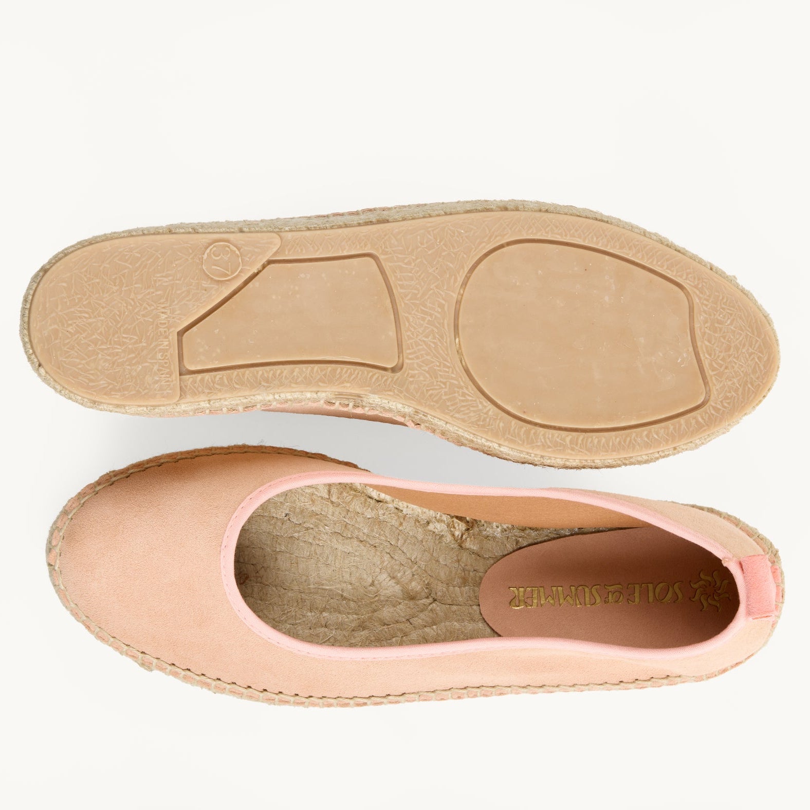 A pair of women's peach suede flat ballet espadrilles. One of the shoes is turned over to show the underneath. It has a full rubber covering and the other shoe shows the inner of the footwear, unlined jute insole and the Sole of Summer logo printed inside.