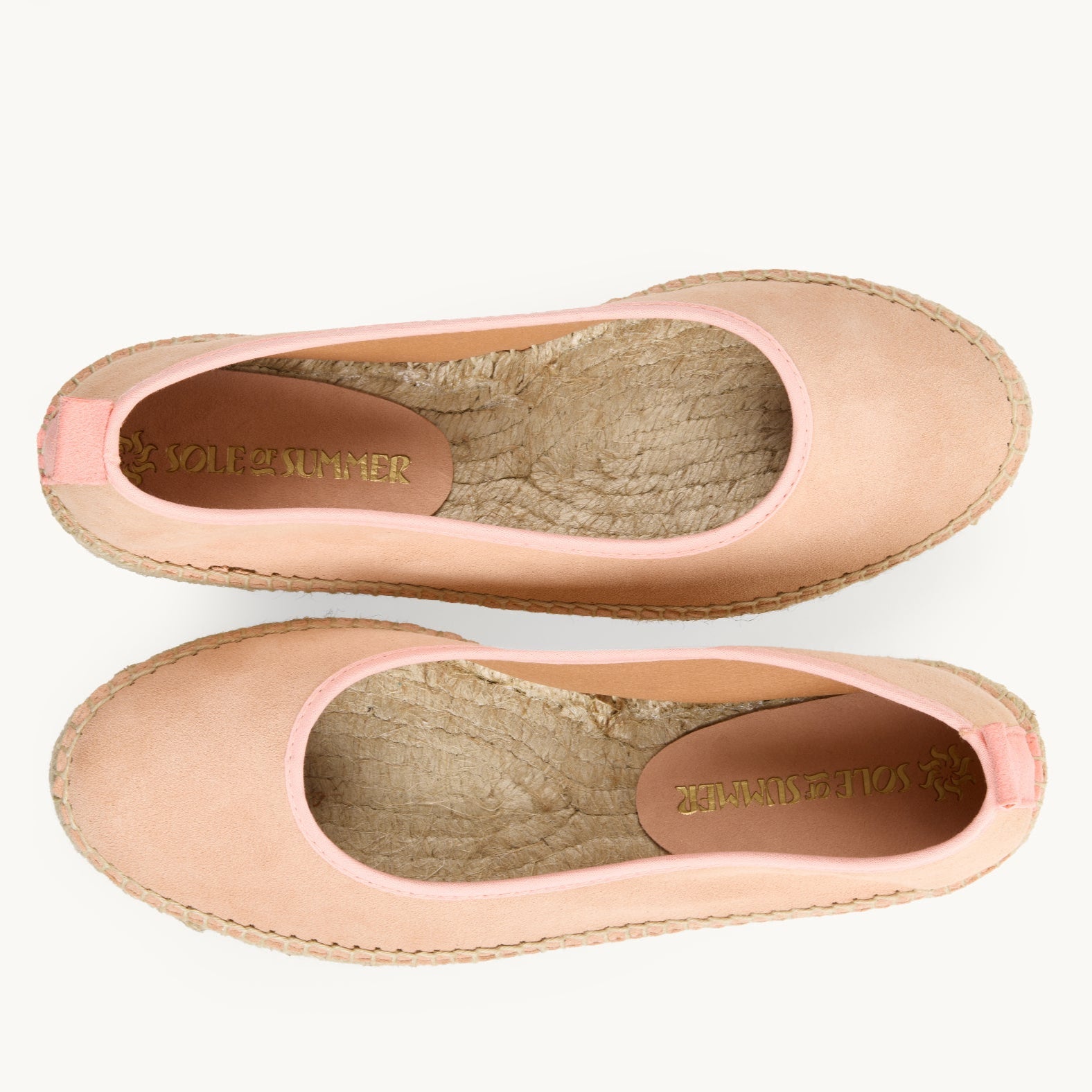 A pair of women's flat ballet espadrilles. View from above looking down on the footwear, unlined jute inside is shown. Peach suede upper with matching cotton trim around the opening of the shoe with stitching around the edge joining the upper to the a traditional jute sole.