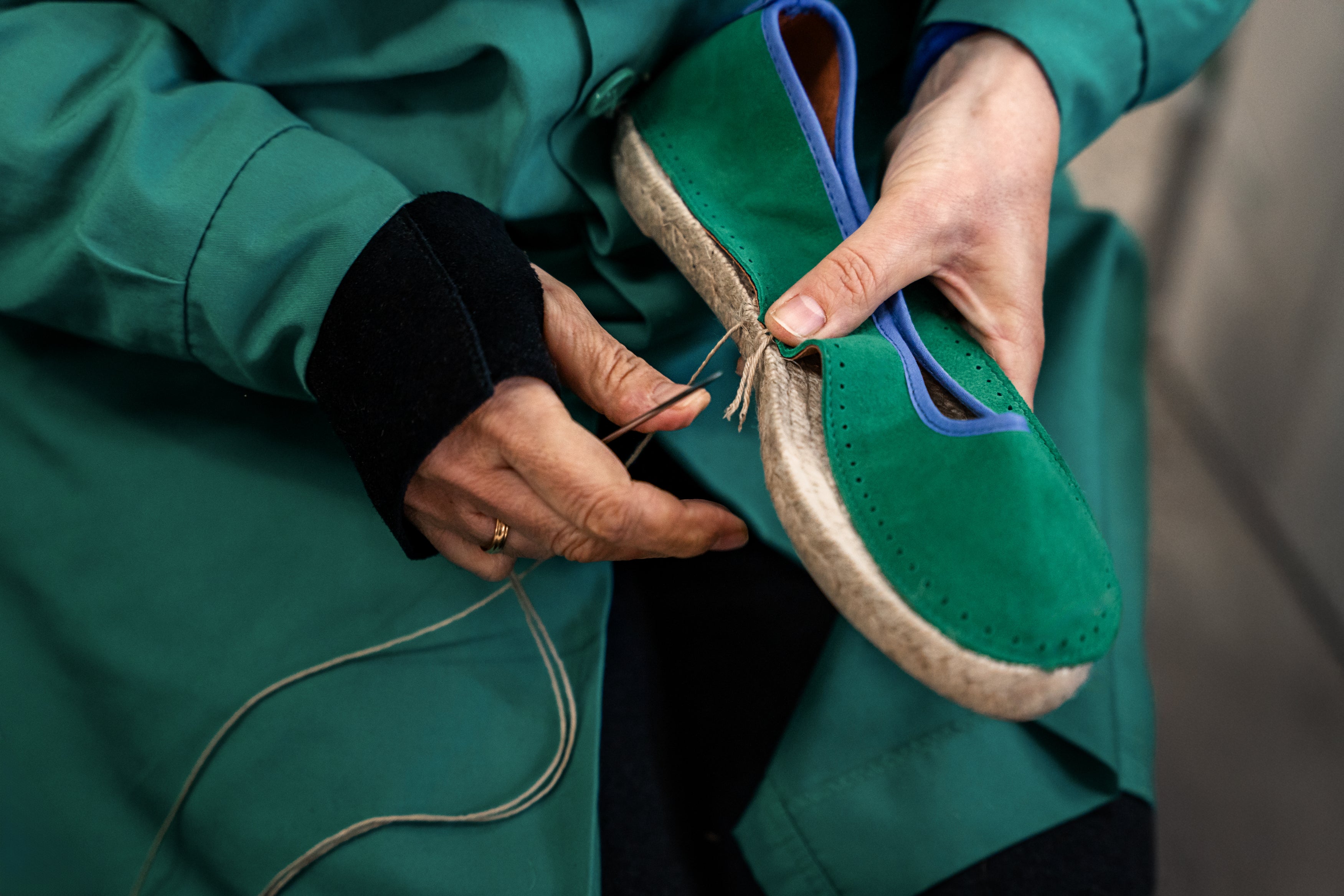 the shoe makers hands are shown sewing the upper of the ballet espadrille to the jute sole using a needle to hand sew traditionally.