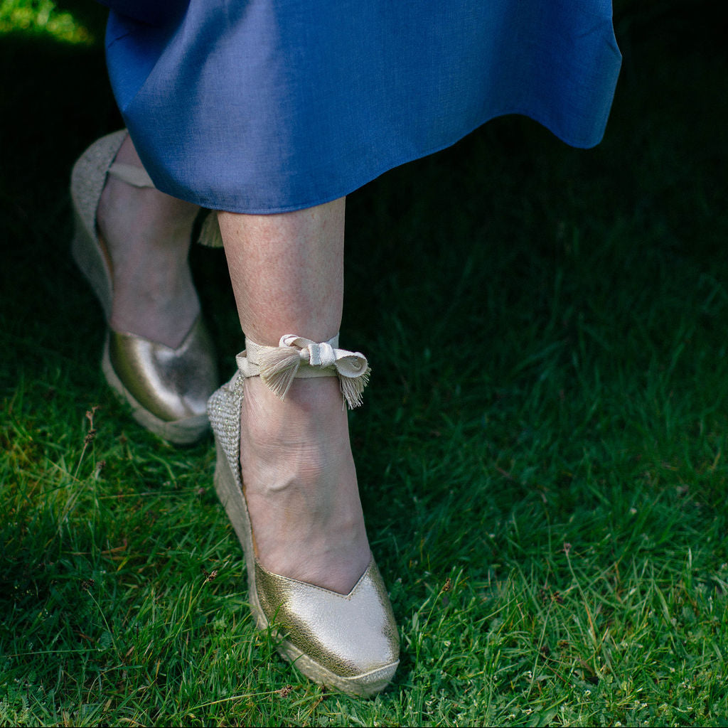 Person wearing gold shoes with ribbons on grass