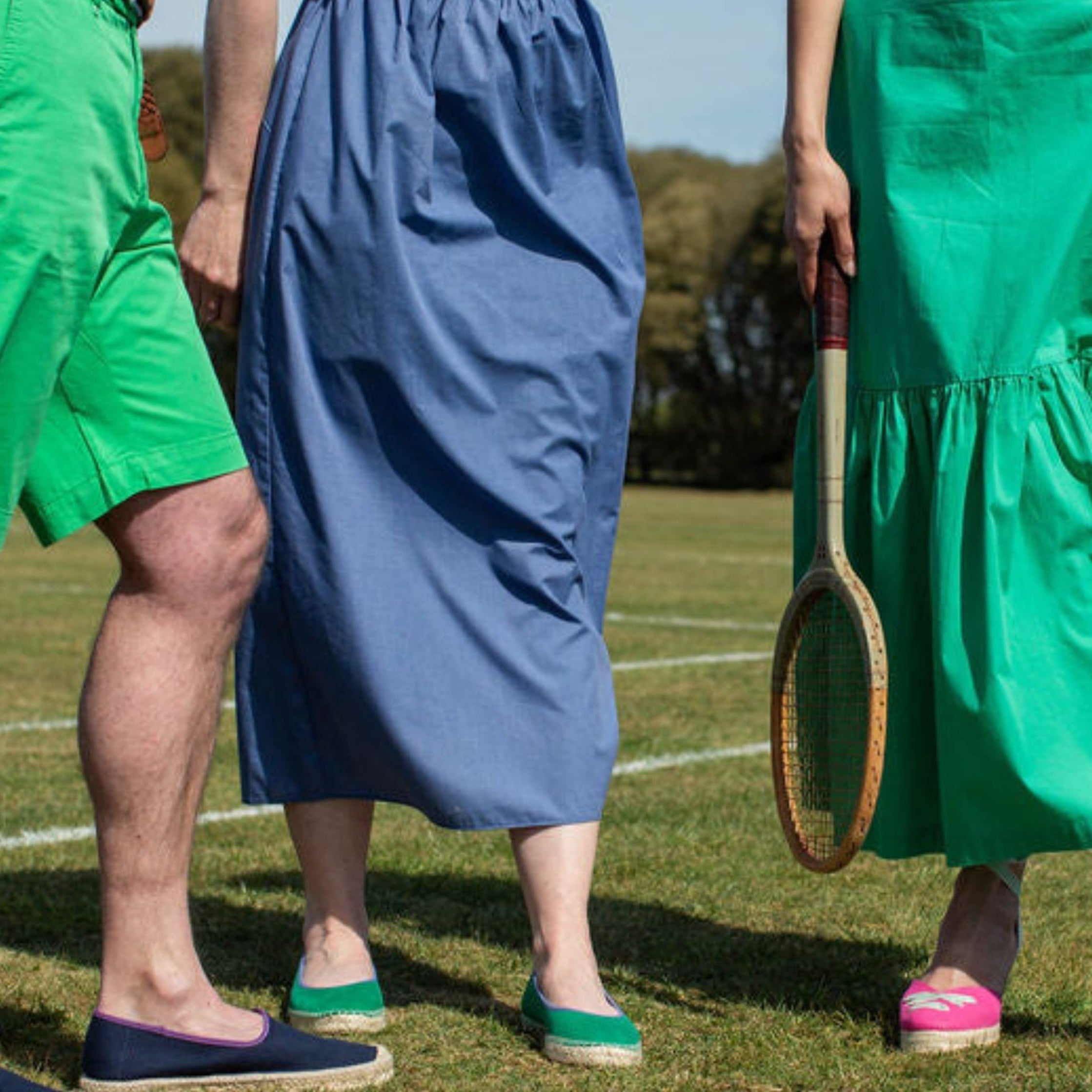Three people on a tennis court wearing colorful clothing and shoes, holding tennis rackets.