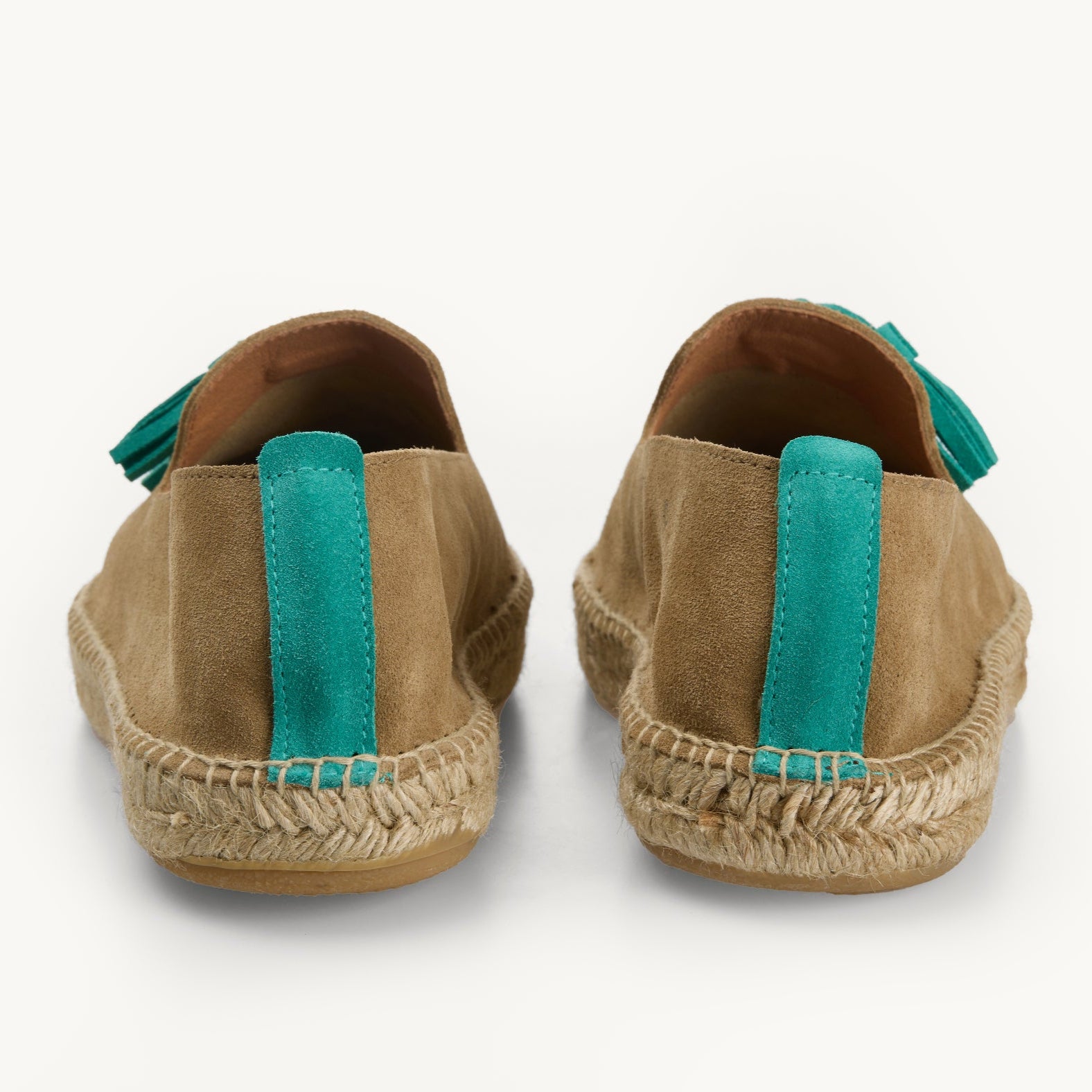 A pair of light tan suede men's  espadrille loafers. Only the back details of the heels are shown. A  stripe of turquoise suede about a centimetre wide runs straight up the back heel. Stitching around the edge of the upper to join it to the  traditional jute sole.  The side of the turquoise tassels are shown.