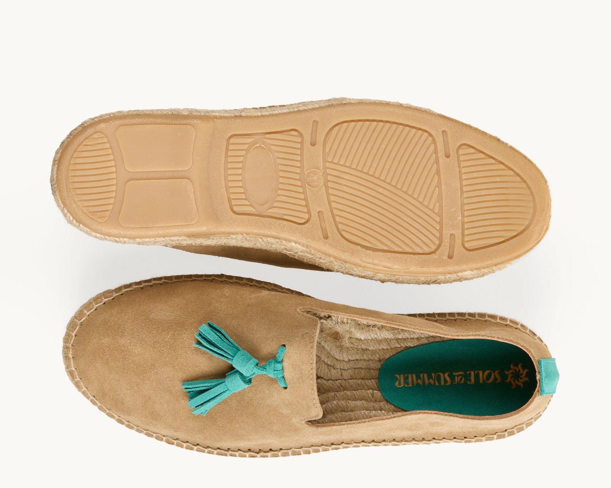 A pair of men's light tan suede loafer espadrilles. One of the footwear is turned over to show the underneath. It has a full rubber covering and the other shoe shows the inner, unlined jute insole and the Sole of Summer logo printed on a small piece of green suede. The other shoe is the right way up and shows the turquoise suede tassels on the front of the footwear and a turquoise suede stripe up the heel.