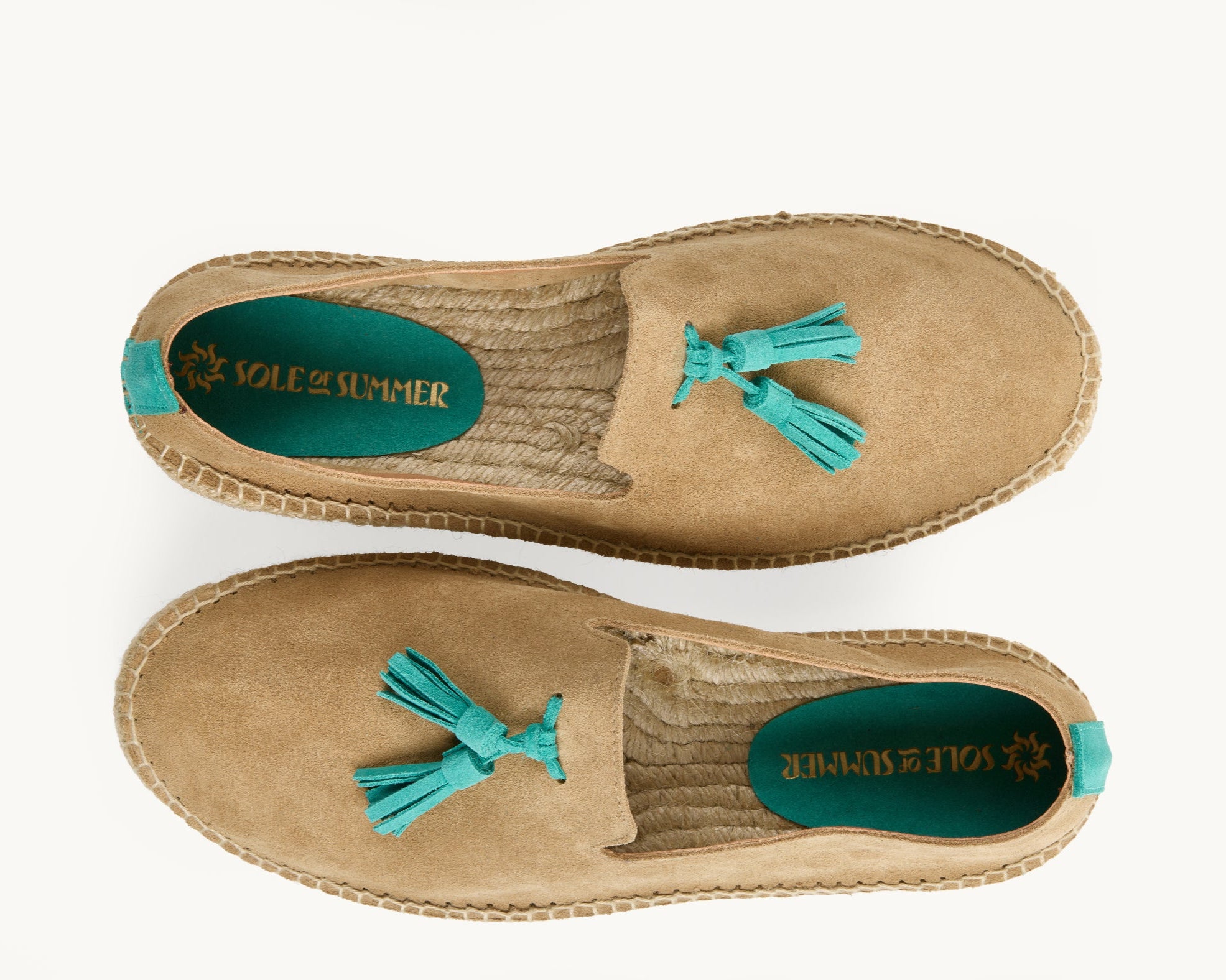 A pair of men's loafer espadrilles.  Arial view. Light tan suede upper with turquoise suede tassels on the front. Insole is unlined, jute inside with a small piece of turquoise suede printed with Sole of Summer logo in gold. Stripe of turquoise suede about 1cm wide up the heels.