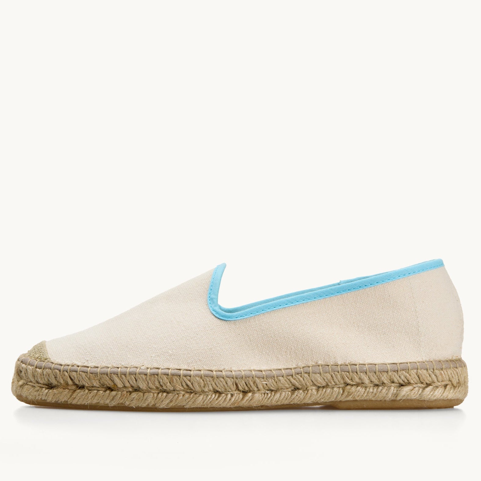 One men's white cotton canvas loafer, side view. Jute sole and detail on the toe. Neck opening of the espadrille has a narrow ribbon edged in light blue.