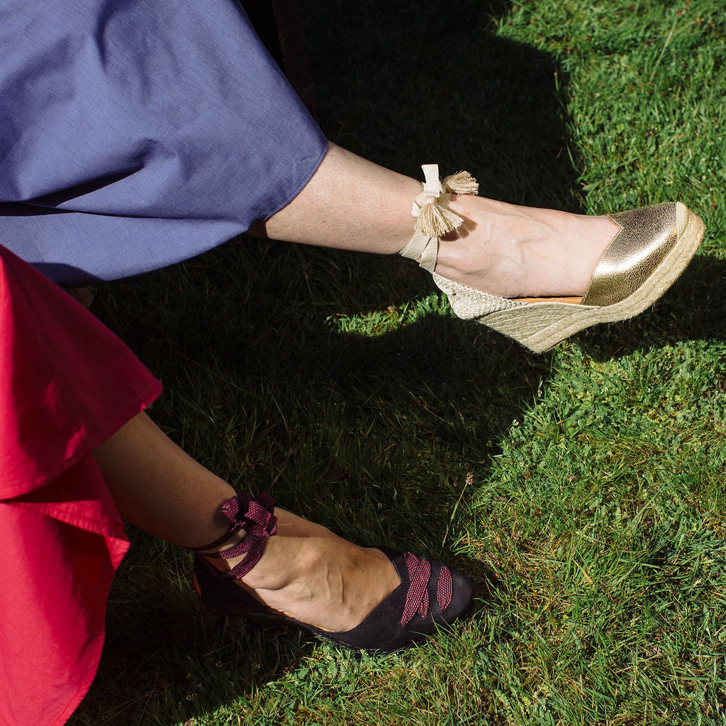 Two pairs of feet wearing gold and black shoes on grass