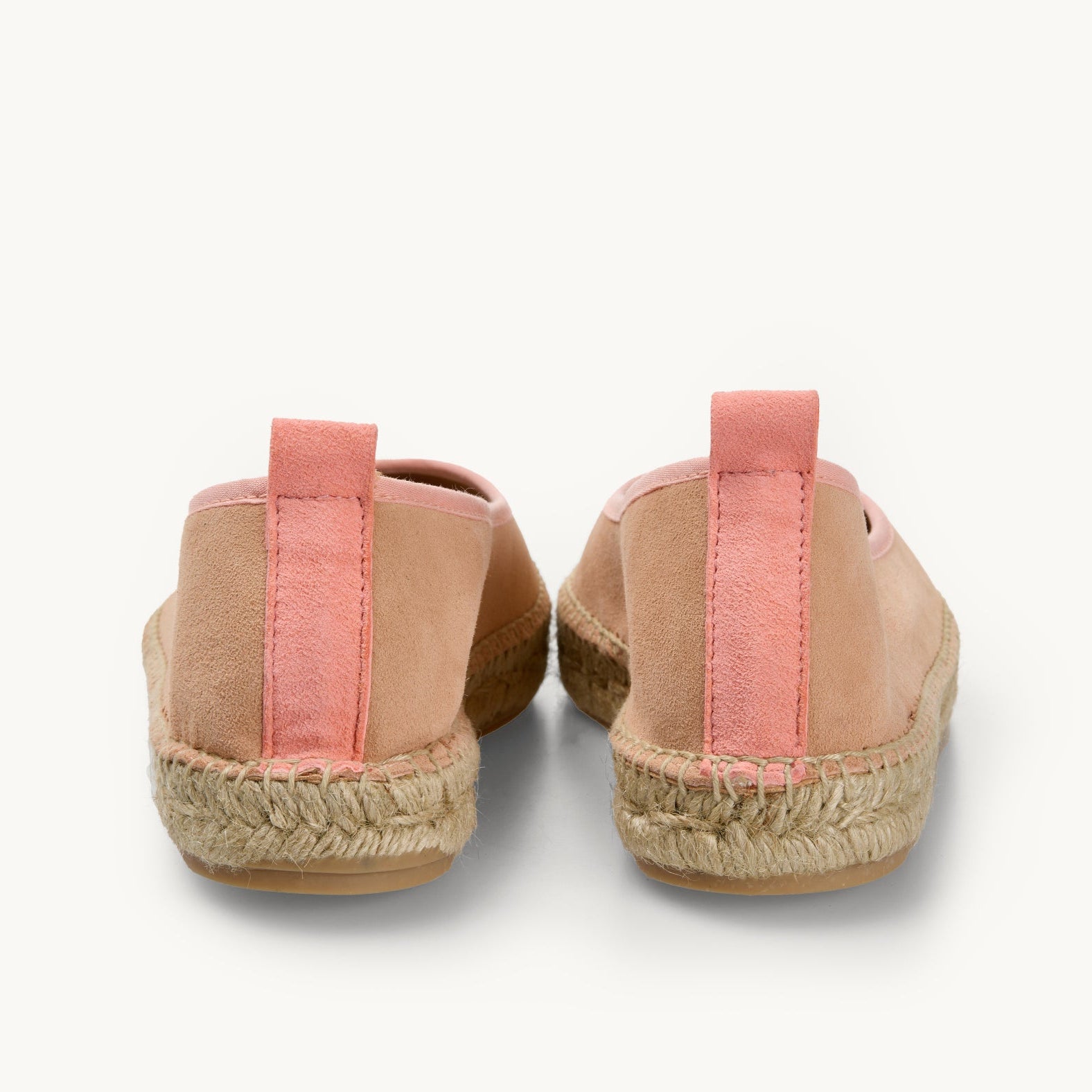 A pair of peach suede women's ballet espadrille flat shoes. Only the back details of the heels are shown. A darker peach suede stripe  about a centimetre wide runs straight up the back heel. Matching cotton trim around the opening of the shoe and stitching around the edge to join the upper to the  traditional jute sole.  