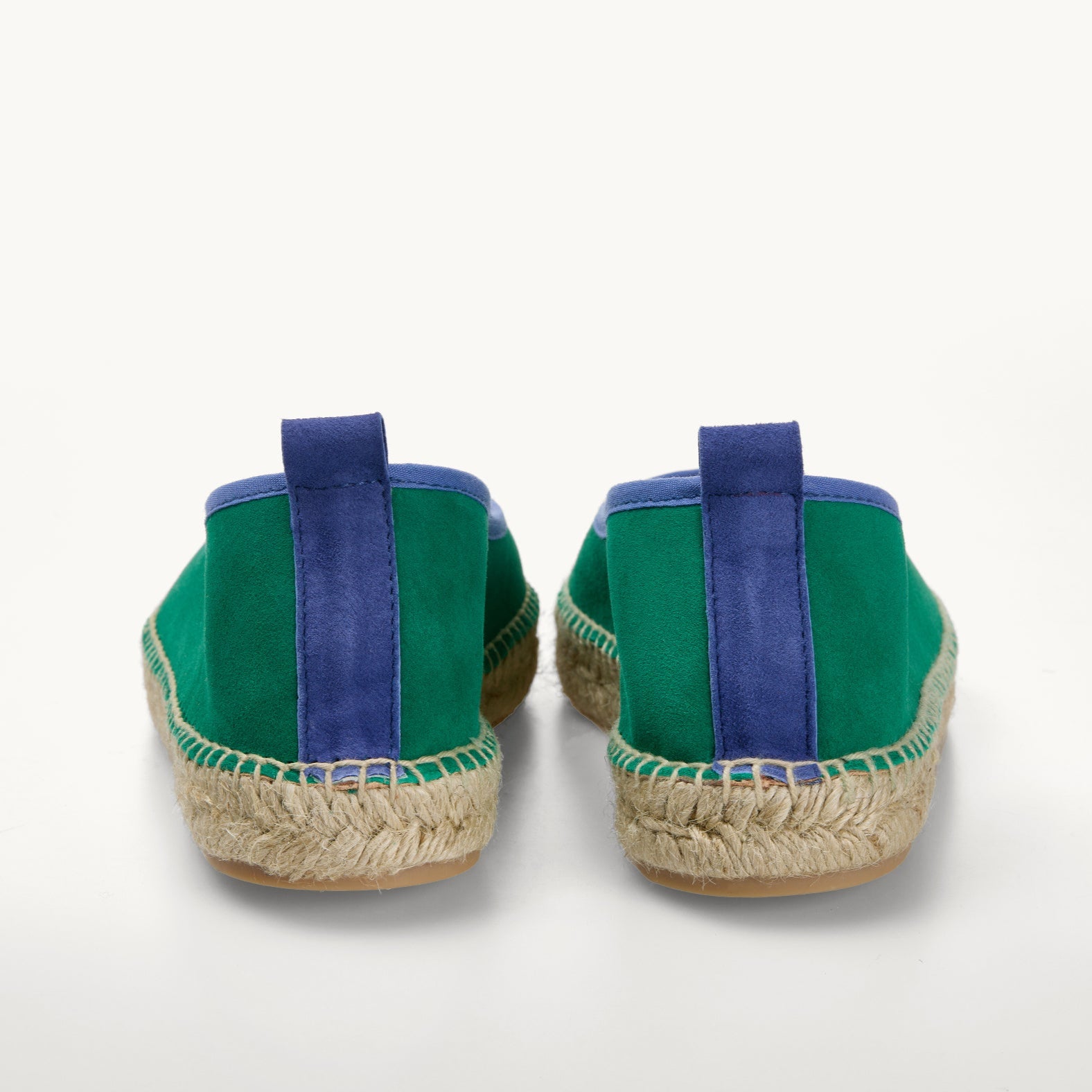 Pair of green suede women's ballet espadrille flat shoes. Only the back details of the heels are shown. A blue suede stripe  about a centimetre wide runs straight up the back heel. Blue cotton trim around the opening of the shoe and stitching around the edge to join the upper to the  traditional jute sole.  