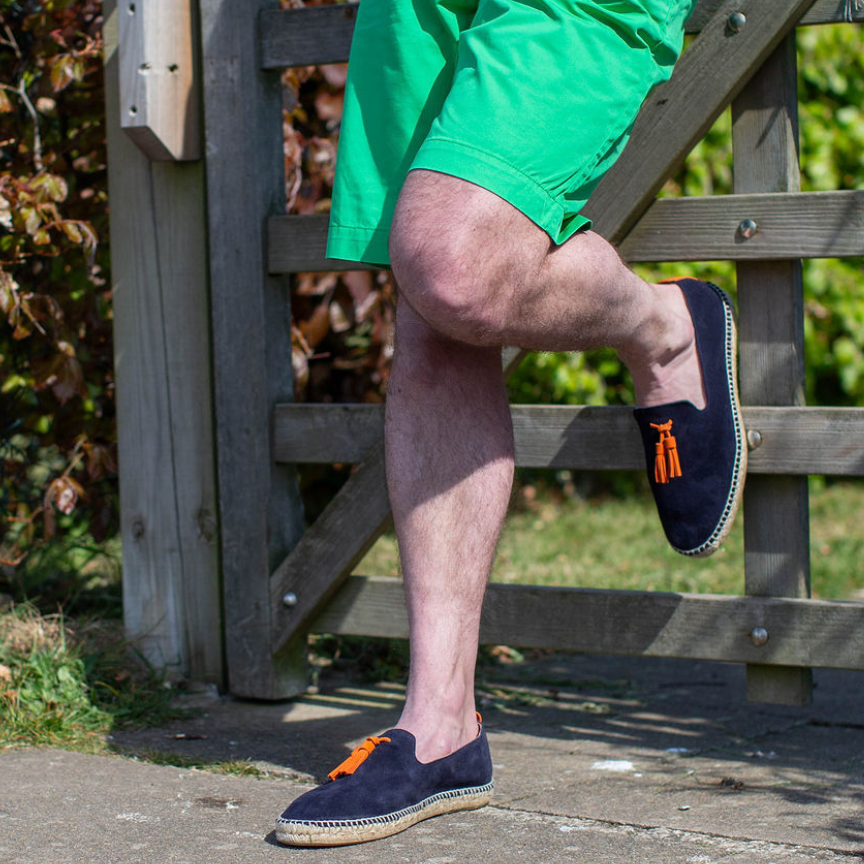 person wearing green shorts wearing navy shoes with orange tassels standing against a wooden gate.