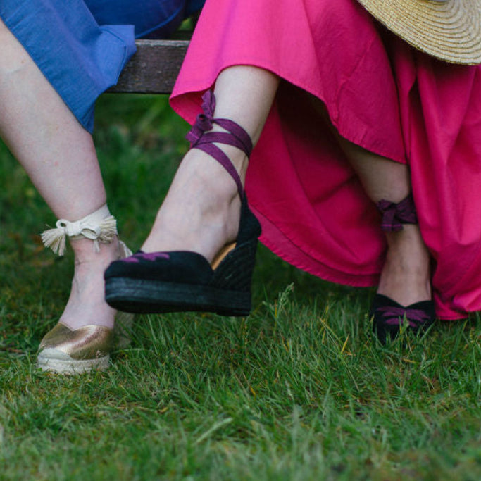 Two people sitting on a bench wearing colorful dresses and shoes with flowers in the background.