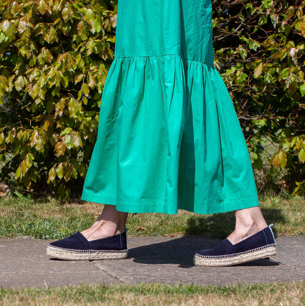 Person wearing a green dress and navy shoes with jute sole on a path with greenery.